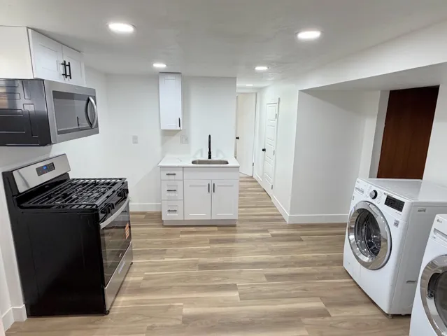 White cabinetry, wood-finish flooring, recessed lighting, and stainless-steel appliances