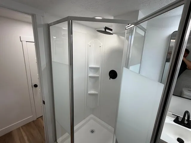 Enclosed shower with a black rain shower head and built-in shelving