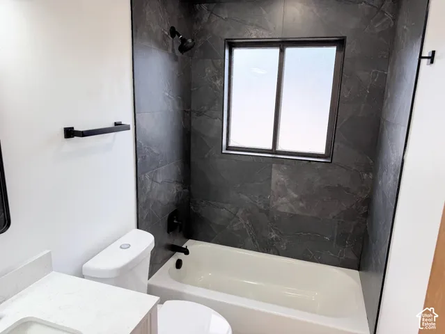 Bathtub with dark-toned tile surround, matte black shower fixtures, frosted window, and a modern toilet
