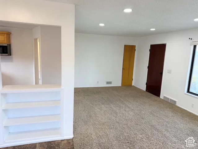 Recessed lighting, light-toned carpeting, built-in shelving, wood cabinetry, and a built-in microwave