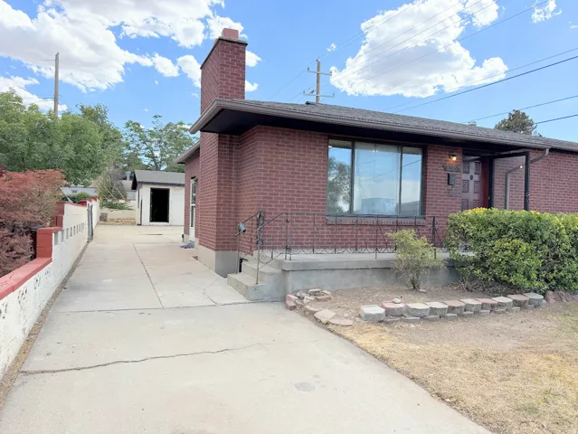 Brick exterior with a prominent chimney, concrete driveway, and front entry with wrought iron railing