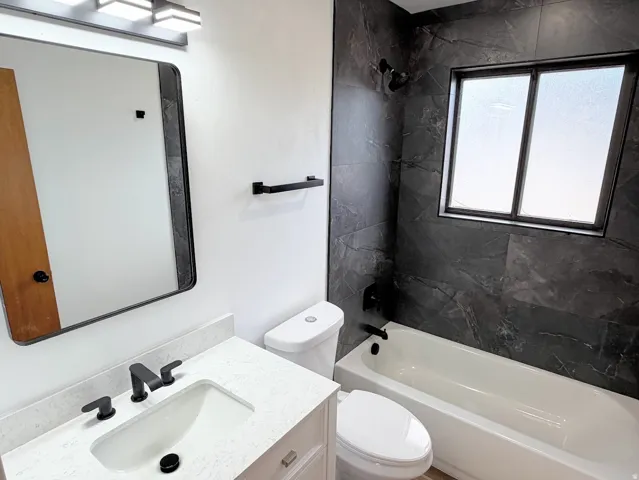 Tub and shower combination with dark tile surround, vanity with light countertop, and black fixtures