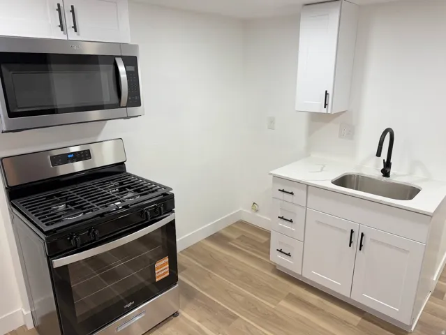 Stainless steel microwave and range, white shaker-style cabinetry, matte black hardware, single-basin sink, and wood-finish flooring