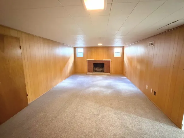 Spacious room featuring carpeting, wood paneling, a brick fireplace, and flush-mount lighting