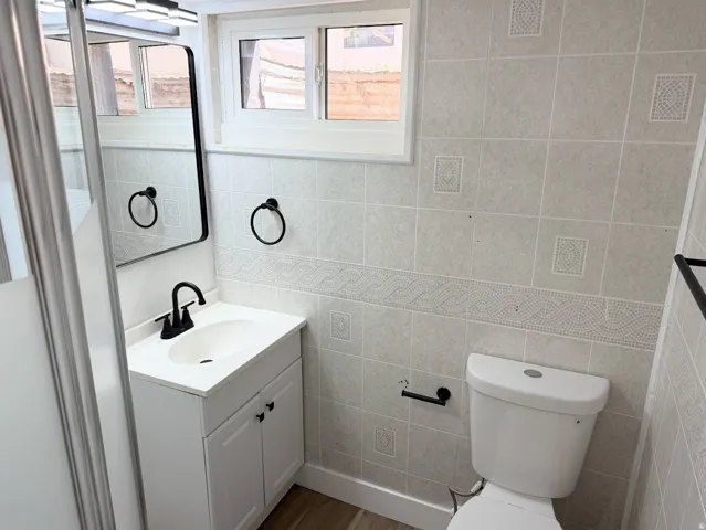 White vanity with matte black hardware, single white sink with matte black faucet, and rectangular black-framed mirror