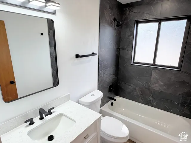 Tub and shower combination with dark tile surround, vanity with light countertop, and black fixtures
