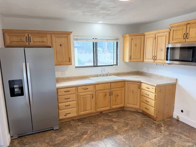 Kitchen featuring a side-by-side refrigerator, wood-finish cabinetry, a built-in microwave, a double basin sink, and laminate countertops