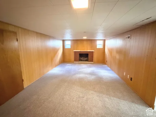 Spacious room featuring carpeting, wood paneling, a brick fireplace, and flush-mount lighting