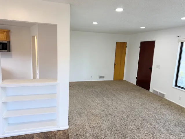 Recessed lighting, light-toned carpeting, built-in shelving, wood cabinetry, and a built-in microwave
