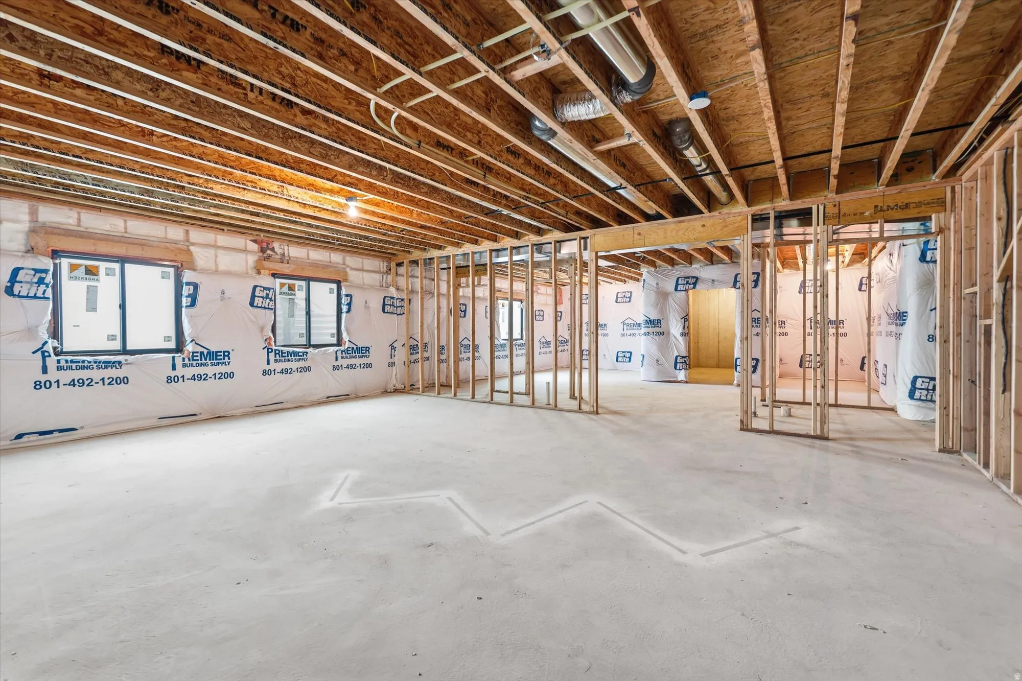 Unfinished basement featuring exposed wood joists, framed interior walls, concrete flooring, and multiple window openings