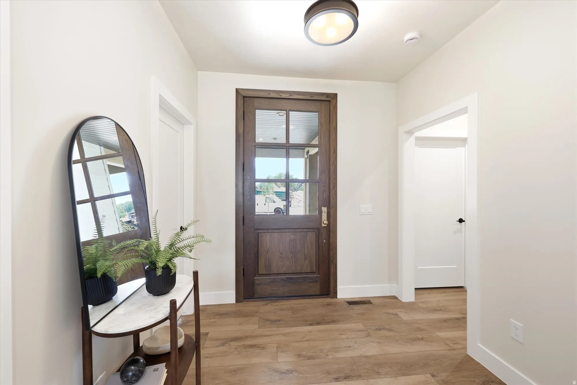 Hardwood-style flooring throughout, with a recessed ceiling light fixture, and a solid wood entry door featuring clear glass panes