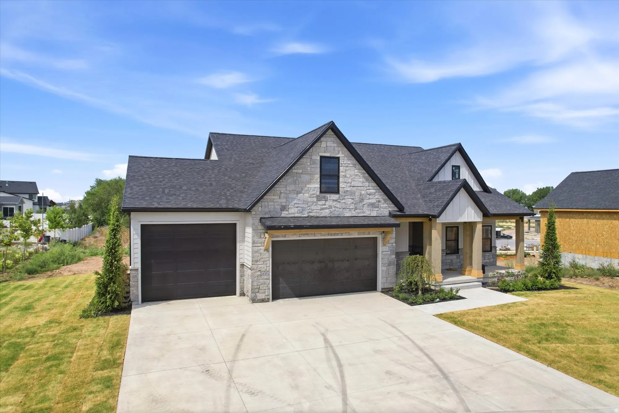 Stone and siding exterior with a dark shingle roof, featuring two attached garage doors, a covered front entry, and a concrete driveway