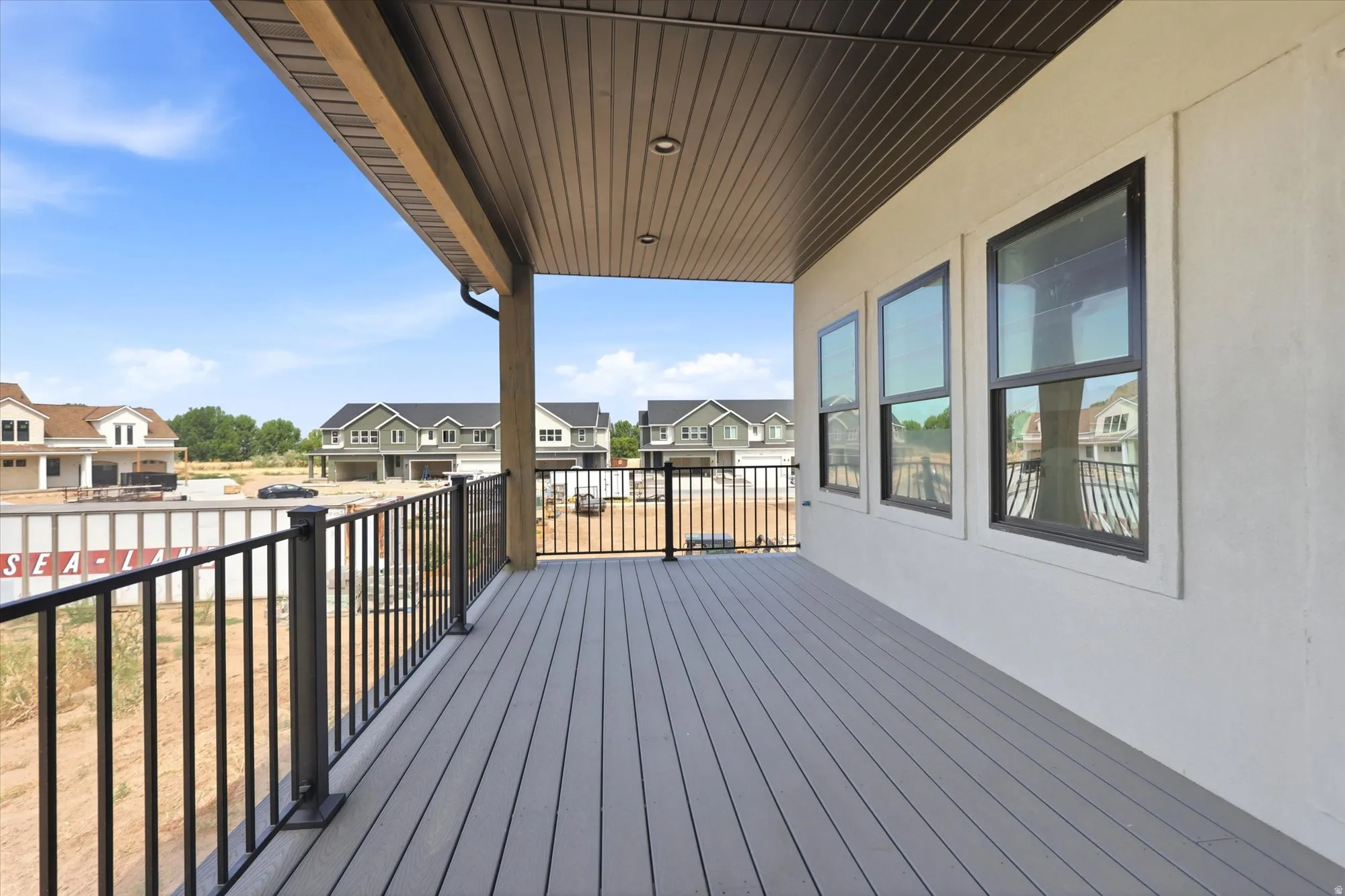 Expansive outdoor deck featuring composite decking, black metal railings, and a solid overhead covering with recessed lighting