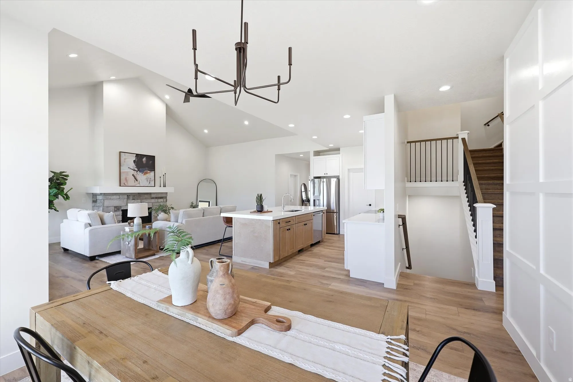 Open concept living area featuring vaulted ceilings, wood-finish flooring, a stone-faced fireplace, and a kitchen island with seating