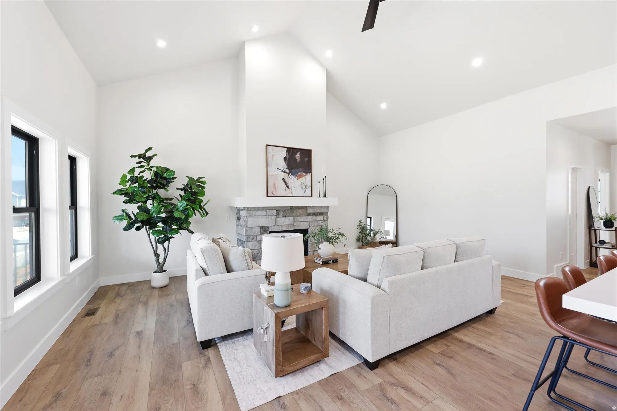 Spacious living area featuring a vaulted ceiling, wood-finish flooring, a stone-clad fireplace, and recessed lighting
