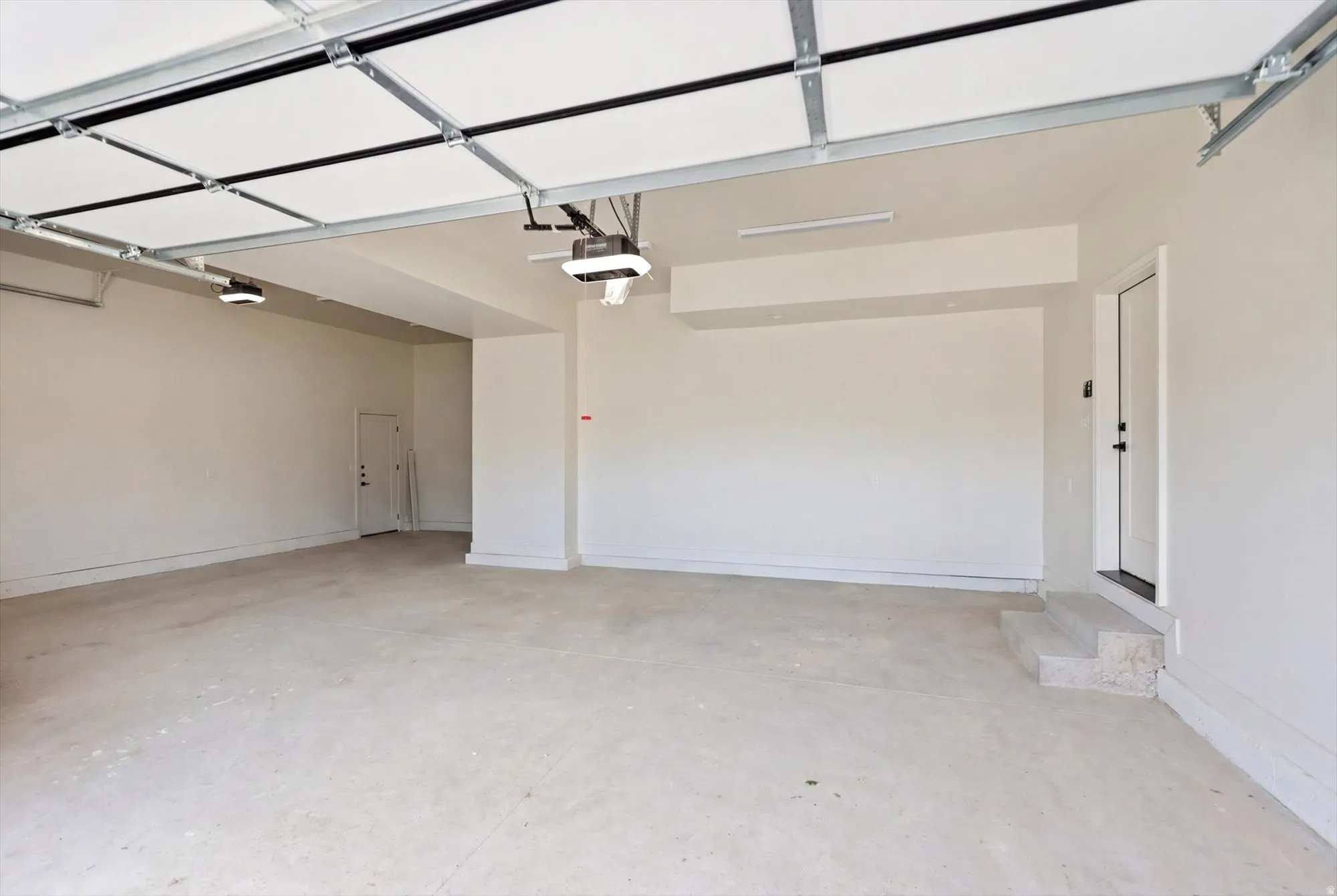 Spacious 3-car garage with light-toned concrete flooring, dual automatic garage door openers, and a white interior access door with steps