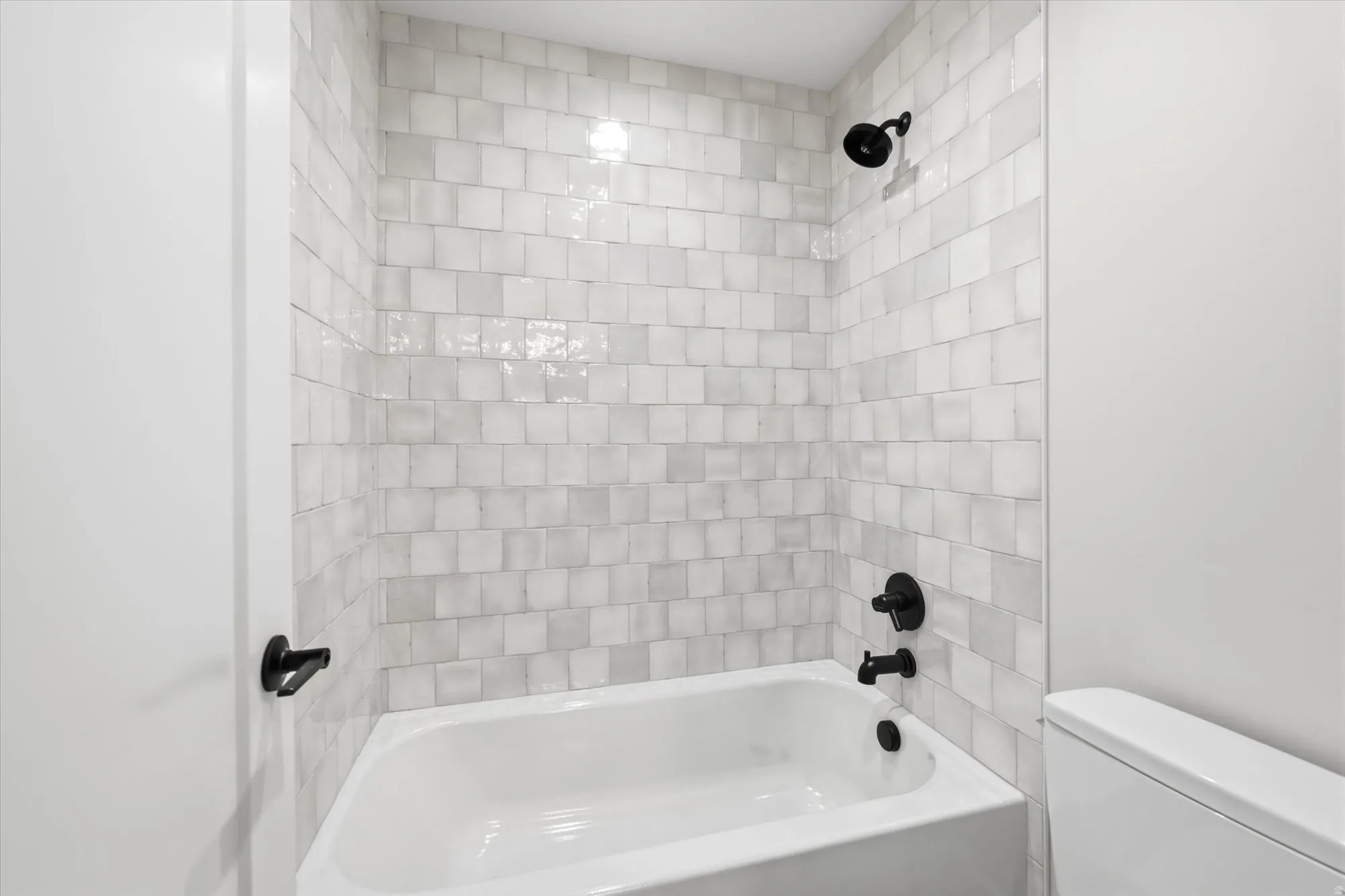 Clean, modern bathroom featuring subway tile surround with contrasting grout lines, a white soaking tub with matte black fixtures, and dual showerheads for versatile bathing options