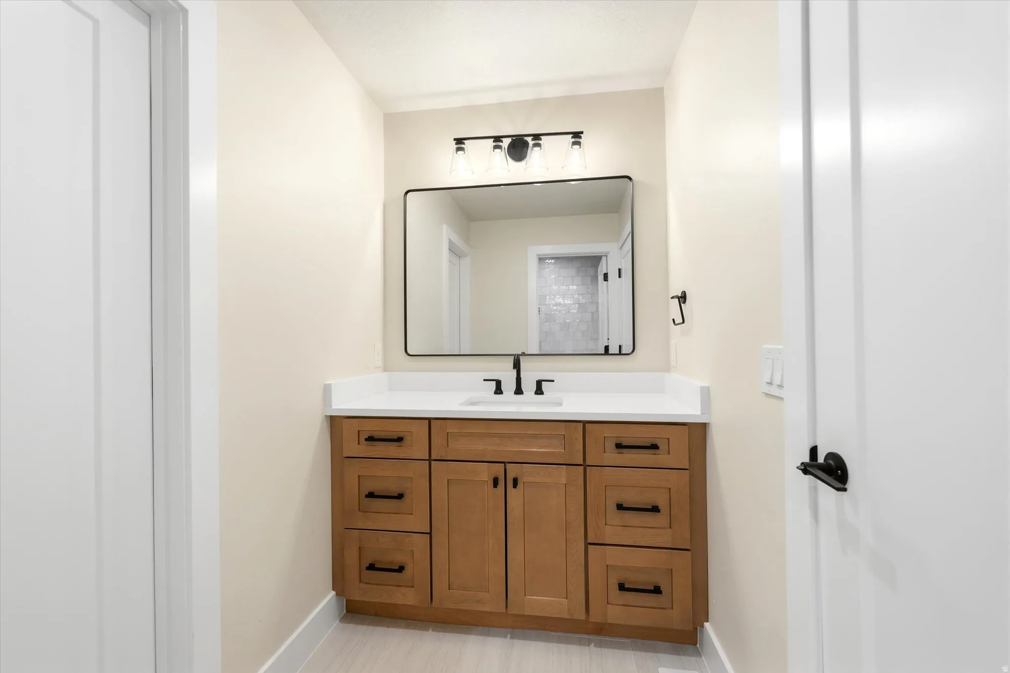 Wood-finish vanity with white countertop, undermount sink, and matte black hardware