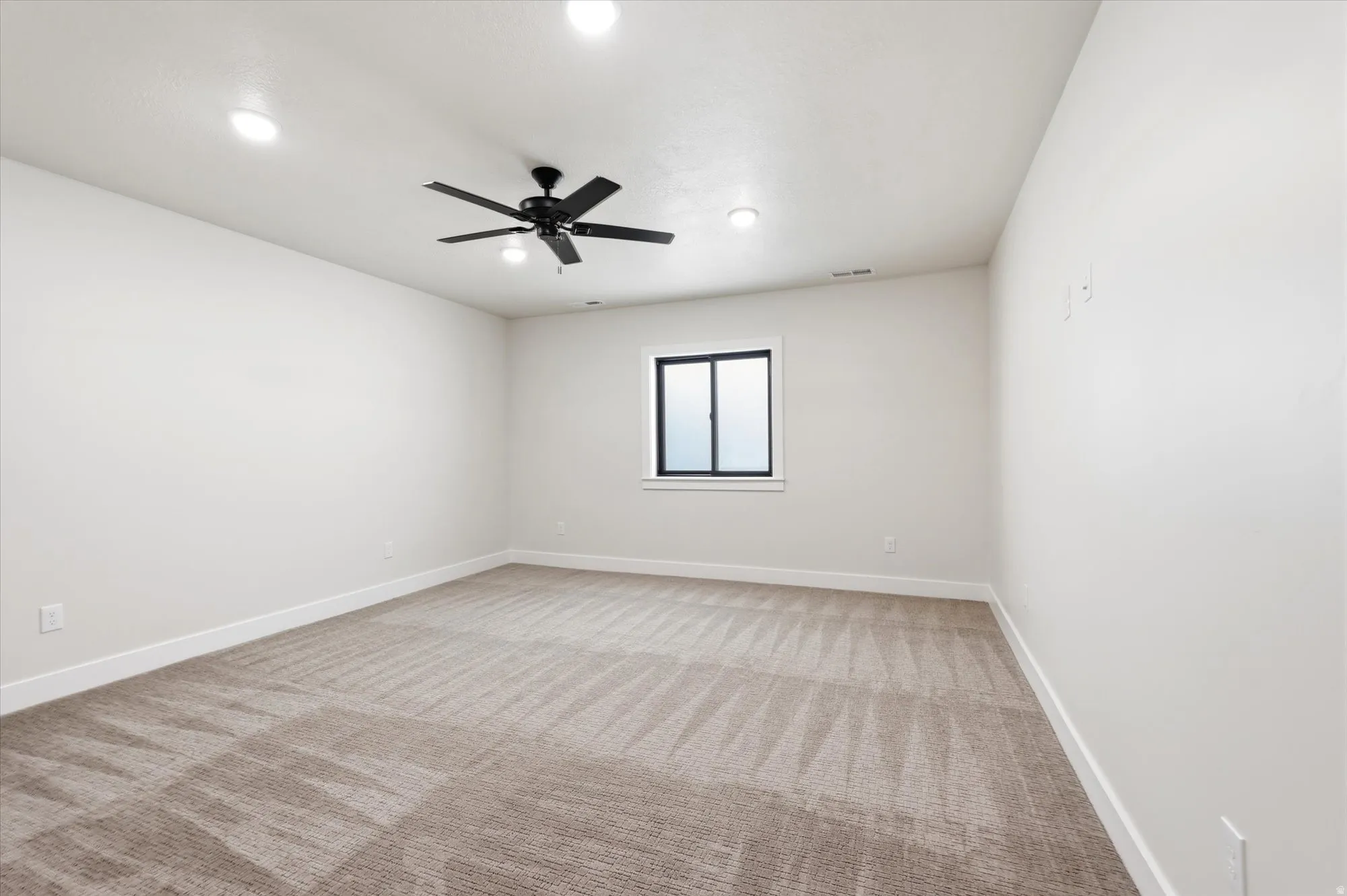 Recessed lighting, ceiling fan with integrated light, neutral carpeting, and a window with black trim