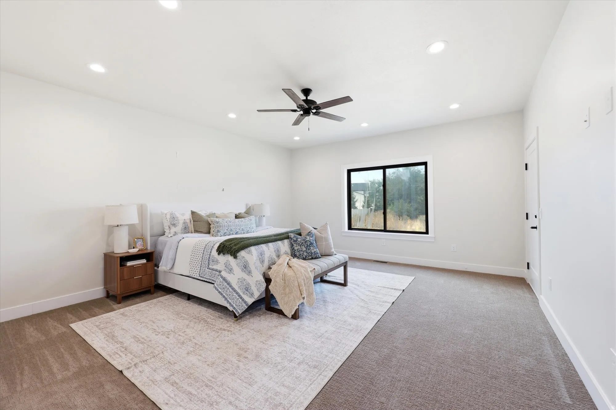 Recessed ceiling lighting, ceiling fan, white paneled doors with matte black hardware, and a large window.