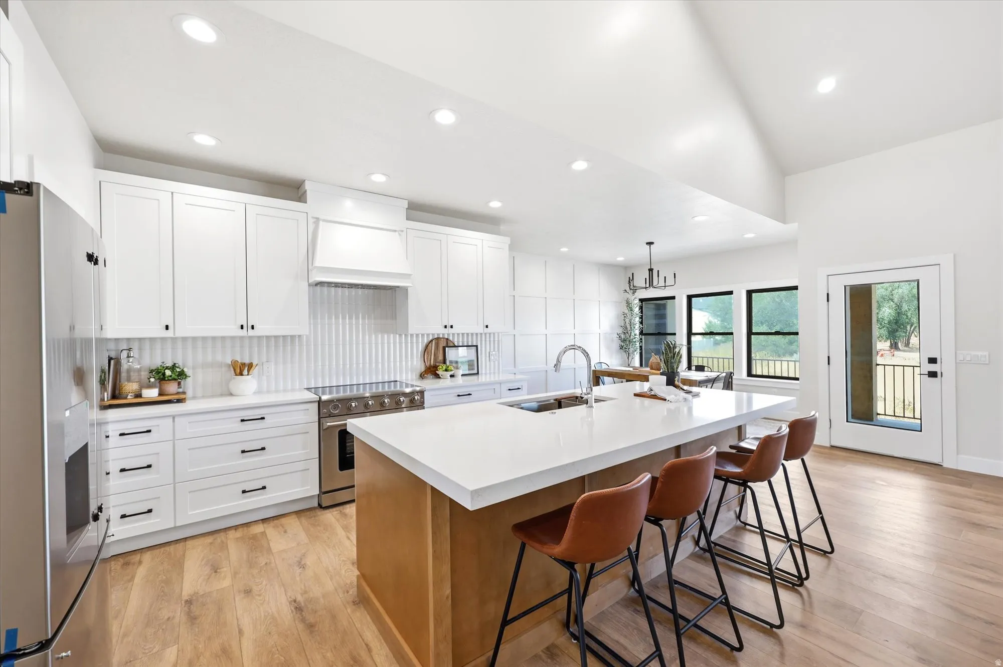 Kitchen featuring white shaker cabinetry, stainless steel appliances, a center island with countertop seating, wood-finish flooring, and a vaulted ceiling