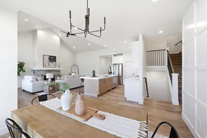 Open concept living area featuring vaulted ceilings, wood-finish flooring, a stone-faced fireplace, and a kitchen island with seating