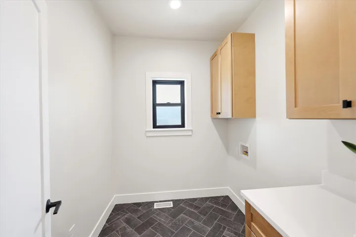Recessed ceiling lighting, a window with black trim, wood-finish cabinetry, a white countertop, and dark herringbone-patterned floor tiles