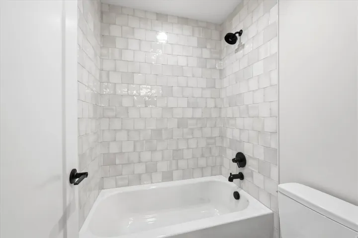 Clean, modern bathroom featuring subway tile surround with contrasting grout lines, a white soaking tub with matte black fixtures, and dual showerheads for versatile bathing options