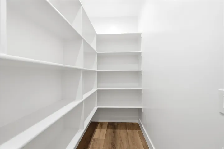 Walk-in pantry featuring extensive white shelving and wood-finish flooring