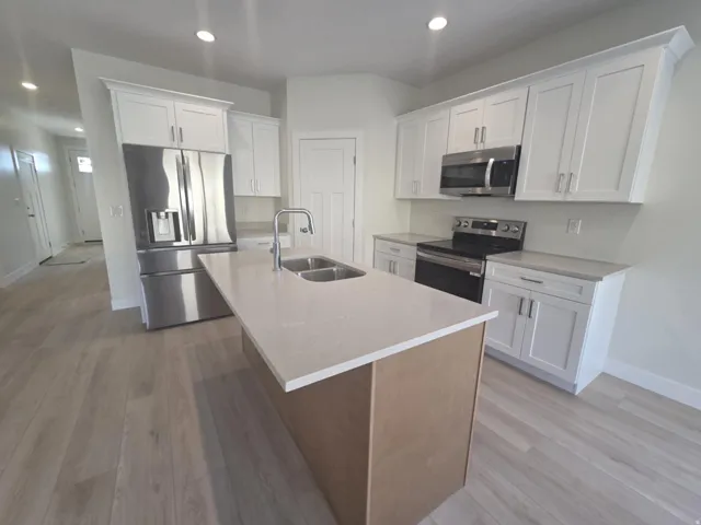 Kitchen featuring a central island with dual sinks and a gooseneck faucet, light-toned countertops, white cabinetry with crown molding, stainless steel appliances, and wood-finish flooring