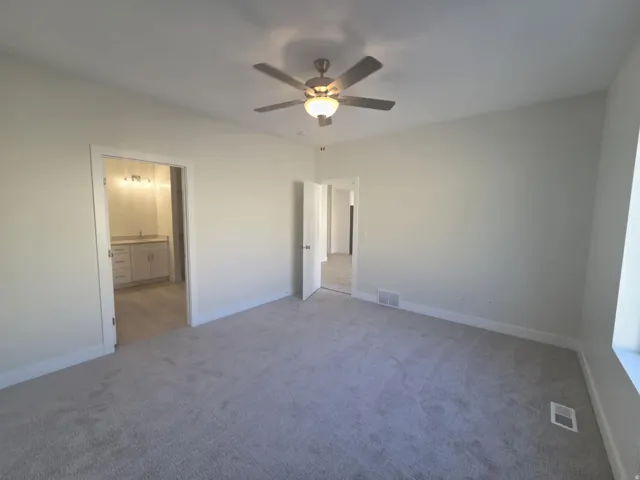 Plush carpeted flooring, a ceiling fan with integrated lighting, and an adjacent bathroom featuring a vanity with a sink and a light fixture