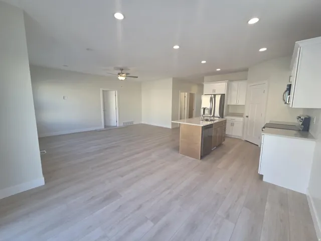 Open-concept living space featuring wood-finish flooring, recessed lighting, a ceiling fan, a kitchen island with seating, and stainless steel appliances