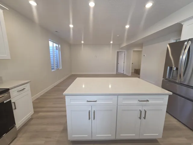 Kitchen island with white shaker cabinetry, light-toned countertop, and recessed lighting