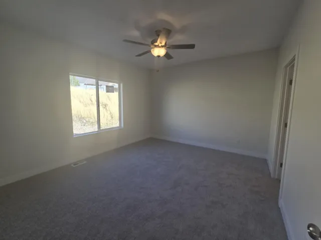 Neutral wall finishes, textured carpet flooring, ceiling fan with integrated lighting, and a single window with white trim