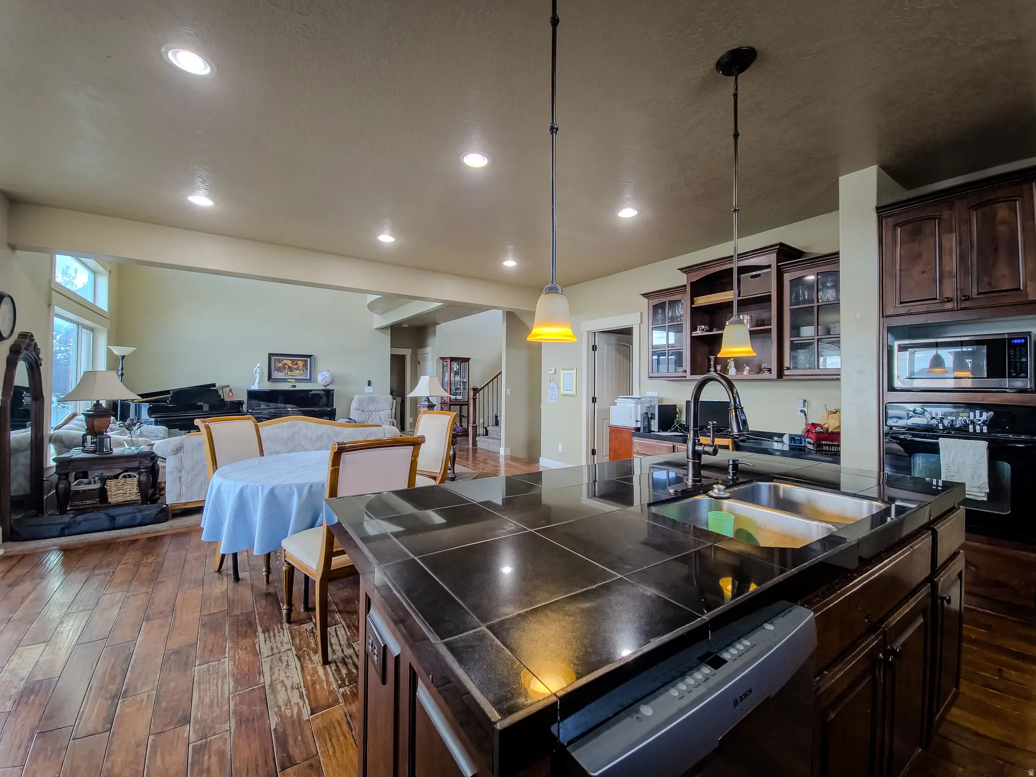 Kitchen featuring dark wood cabinetry, a dual basin stainless steel sink, black tile countertops, and pendant lighting