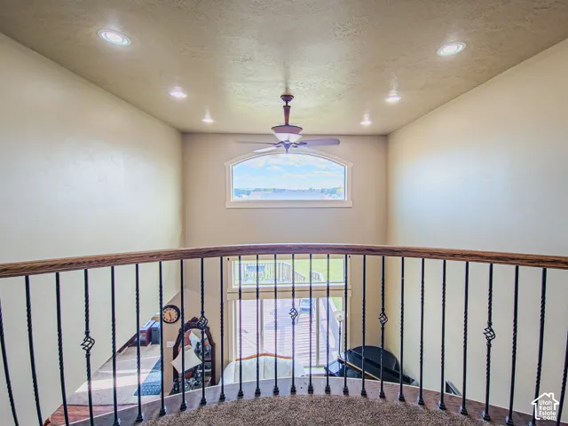 Upper-level landing featuring a wood-finish handrail with wrought iron balusters, recessed ceiling lighting, a ceiling fan, and an arched window