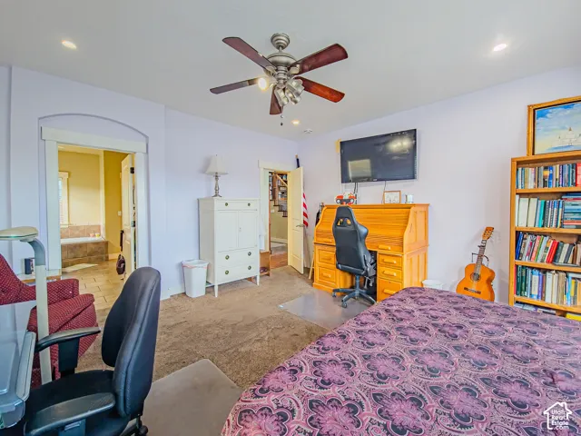 Carpeted room featuring an arched doorway, ceiling fan, built-in shelving, and a wall-mounted television