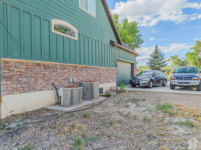 Stone veneer siding with vertical paneling, arched window, and attached garage with paved driveway