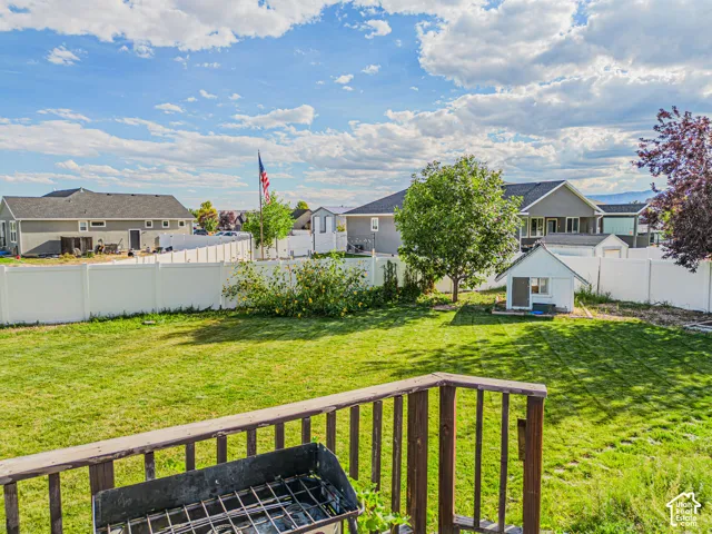 Expansive backyard featuring a manicured lawn, mature trees, a white privacy fence, and a detached storage shed
