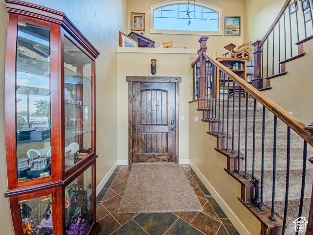 Vaulted ceiling with an arched window, wood-finish door, tile flooring, and a carpeted staircase with wrought iron balusters and a wood handrail