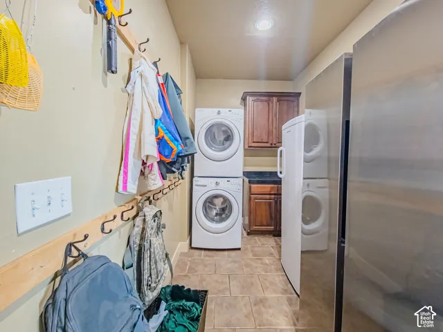 Stacked washer and dryer, stainless steel refrigerator, dark wood-finish cabinetry, tile flooring, and recessed ceiling lighting