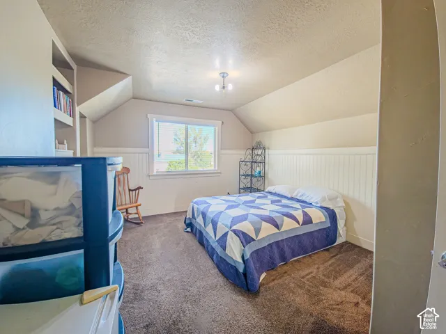 Angled ceiling with a central ceiling light fixture, window with horizontal blinds, built-in shelving, and wainscoting