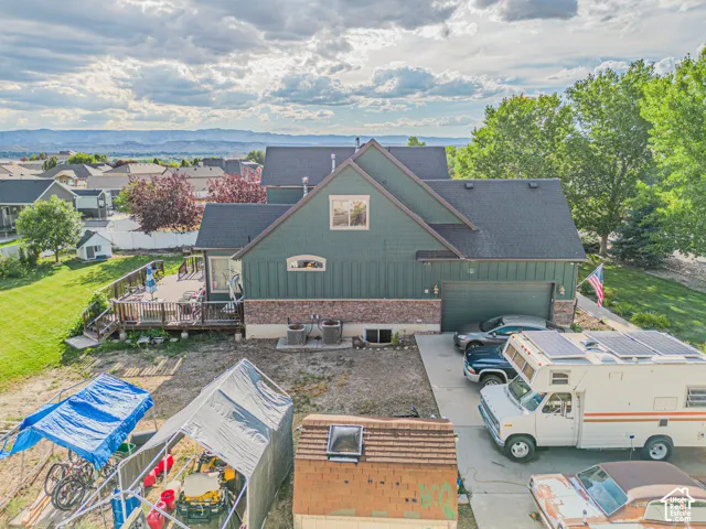 Multi-level residence featuring a dark green siding and brick veneer exterior, a dark shingle roof, an attached garage, a tiered wood deck, and a paved driveway