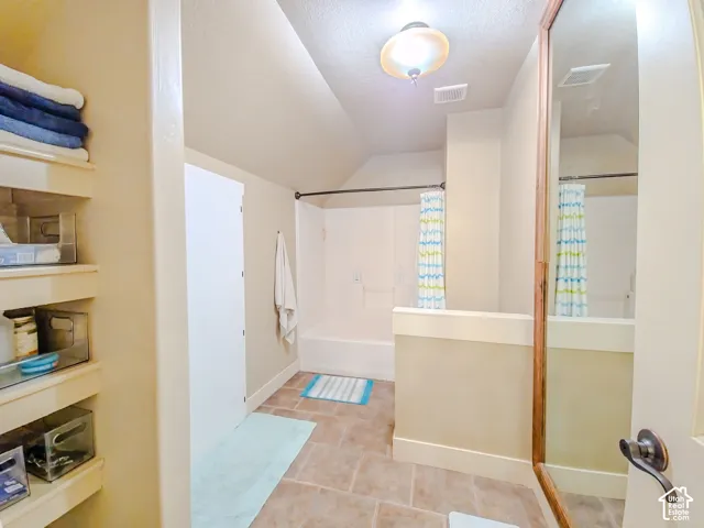Built-in open shelving, tiled flooring, built-in bathtub with shower, and a full-height wall mirror