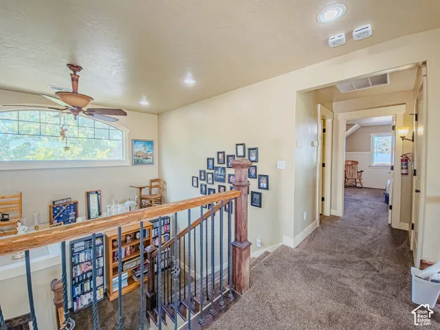 Upper-level landing with carpeted flooring, a wood and wrought iron staircase railing, and recessed lighting
