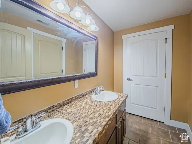 Double vanity with undermount sinks, mosaic tile countertop, chrome fixtures, and a large framed mirror with overhead lighting