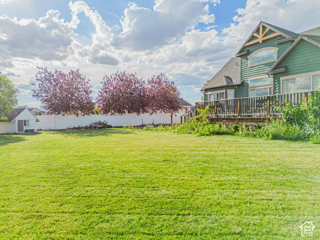 Expansive grassy yard with a white privacy fence and mature trees