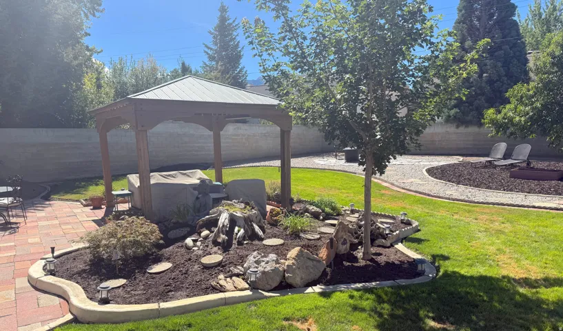 Expansive backyard featuring a wood-frame gazebo, paver patio, and stone-lined pathways