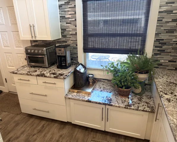 White cabinetry with brushed nickel pulls, wood-finish flooring, mosaic tile backsplash, and stone-finish countertops