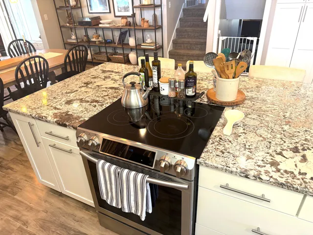 Kitchen island featuring a built-in stainless steel electric range, granite countertops, and white cabinetry with brushed nickel hardware
